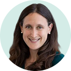 Smiling woman with long dark hair and pearl earrings, wearing a black top.