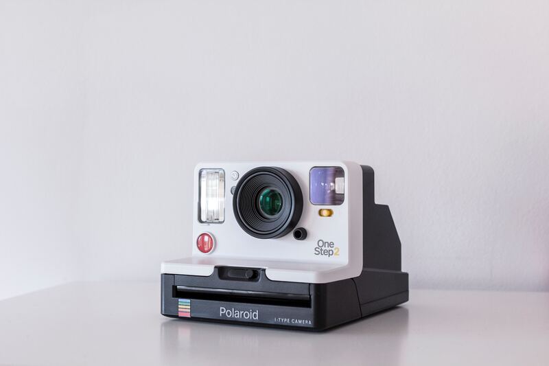 white and black Polaroid One Step 2 instant camera on white board
