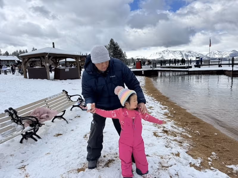 The founding team member, the Cal graduate, of ai fun lab is showing his daughter how to throw a snow ball in Lake Tahoe