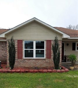 Red colonial shutters fixed to the front of a reddish brick home with tall green bushes on both sides