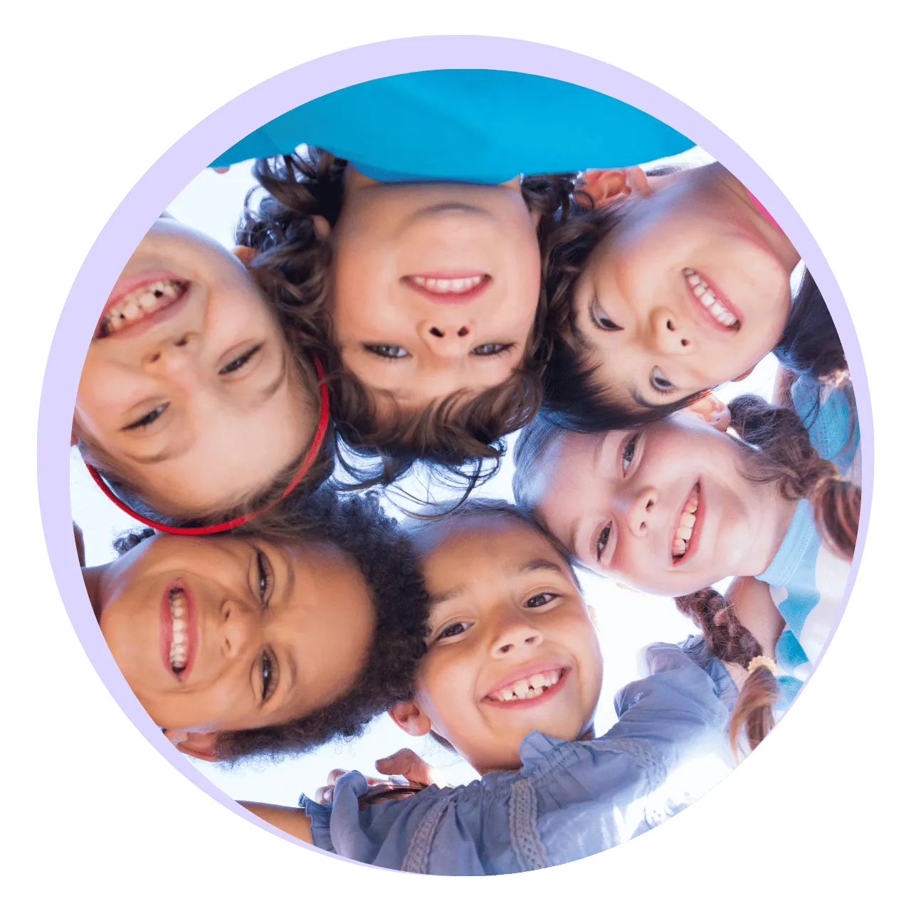Group of six smiling children with heads close together, looking down at the camera in a circle.