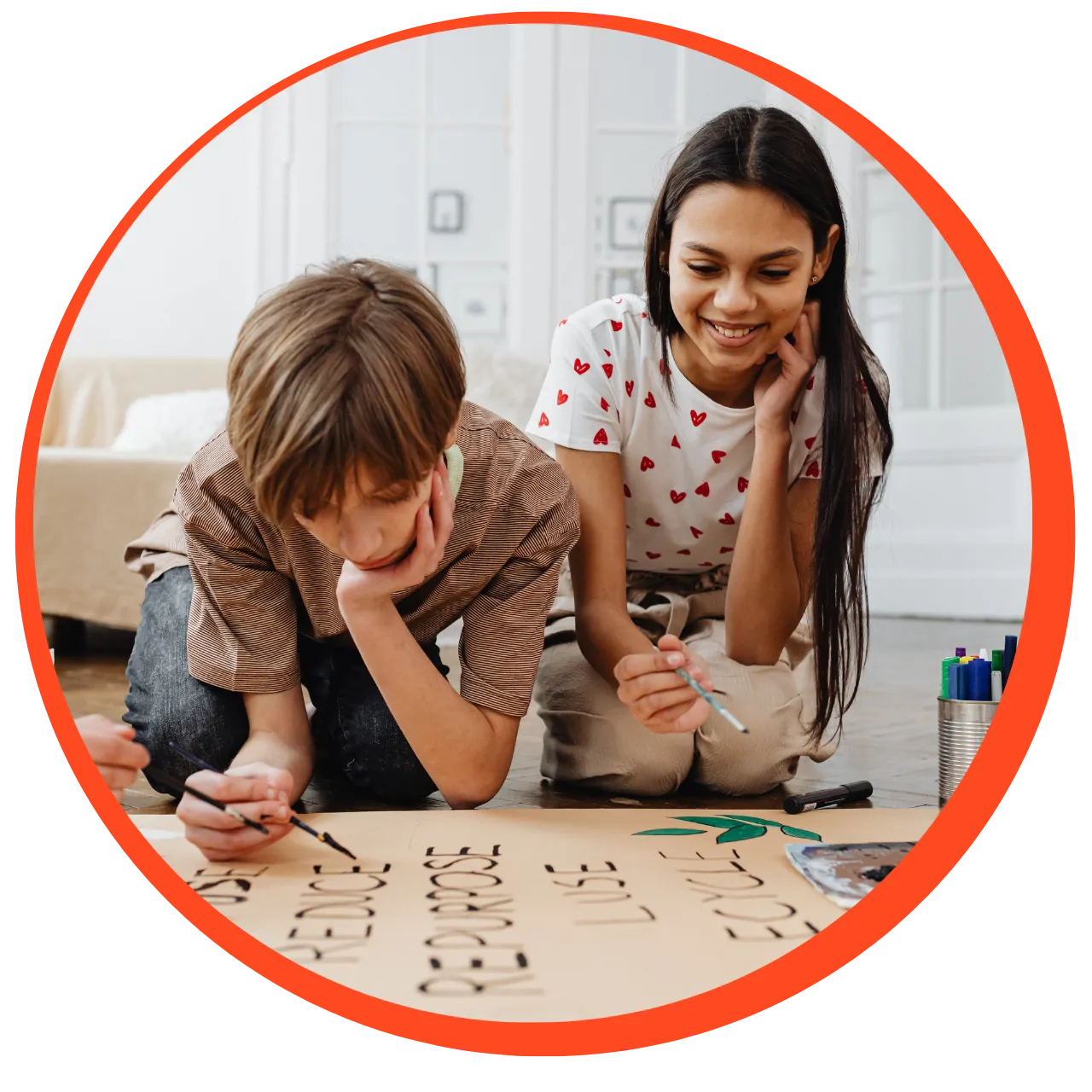 Two children kneeling on the floor painting a poster with words and a green leaf illustration.