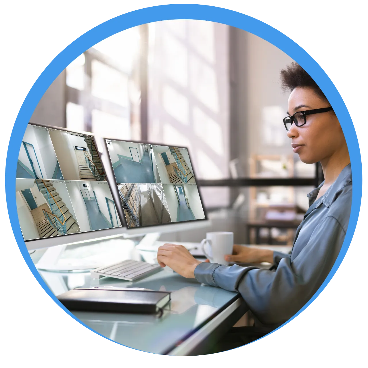 Woman wearing glasses monitoring security camera footage displayed on dual computer screens in a bright office.