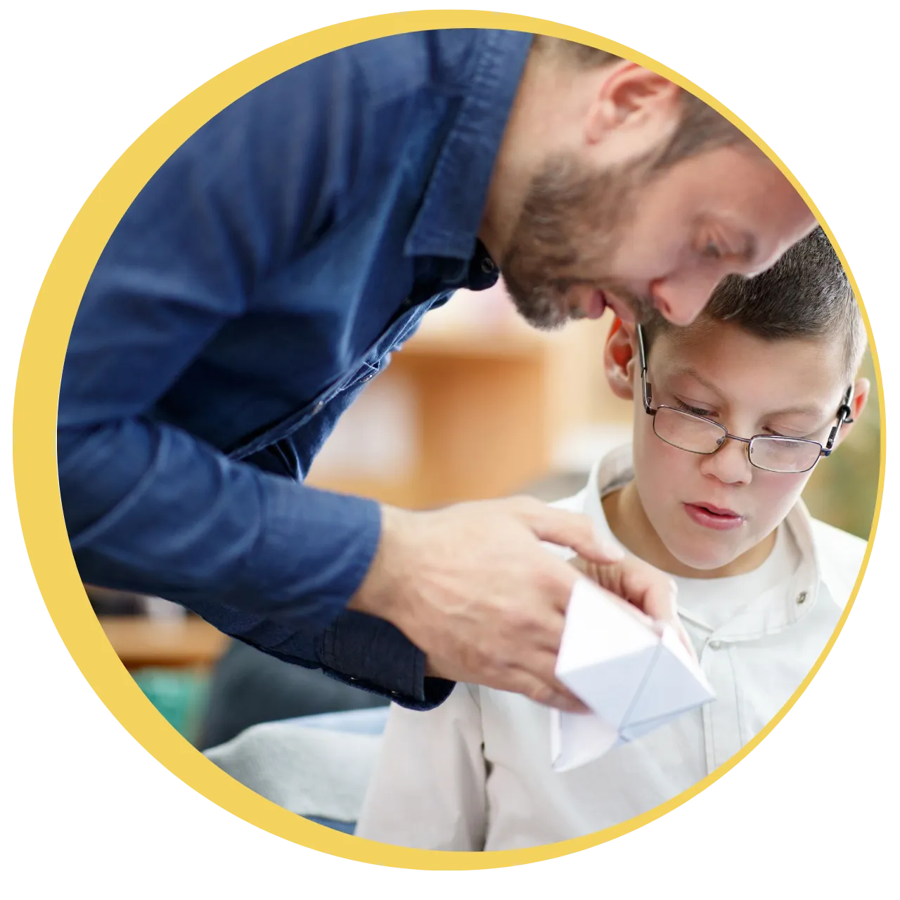 Adult male showing a paper craft to a young boy with glasses, both focused on the object.