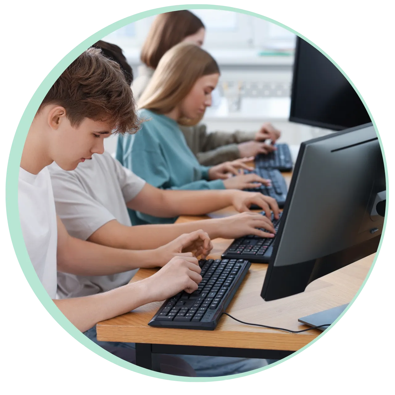 Teenagers focused on typing on keyboards in a computer lab.