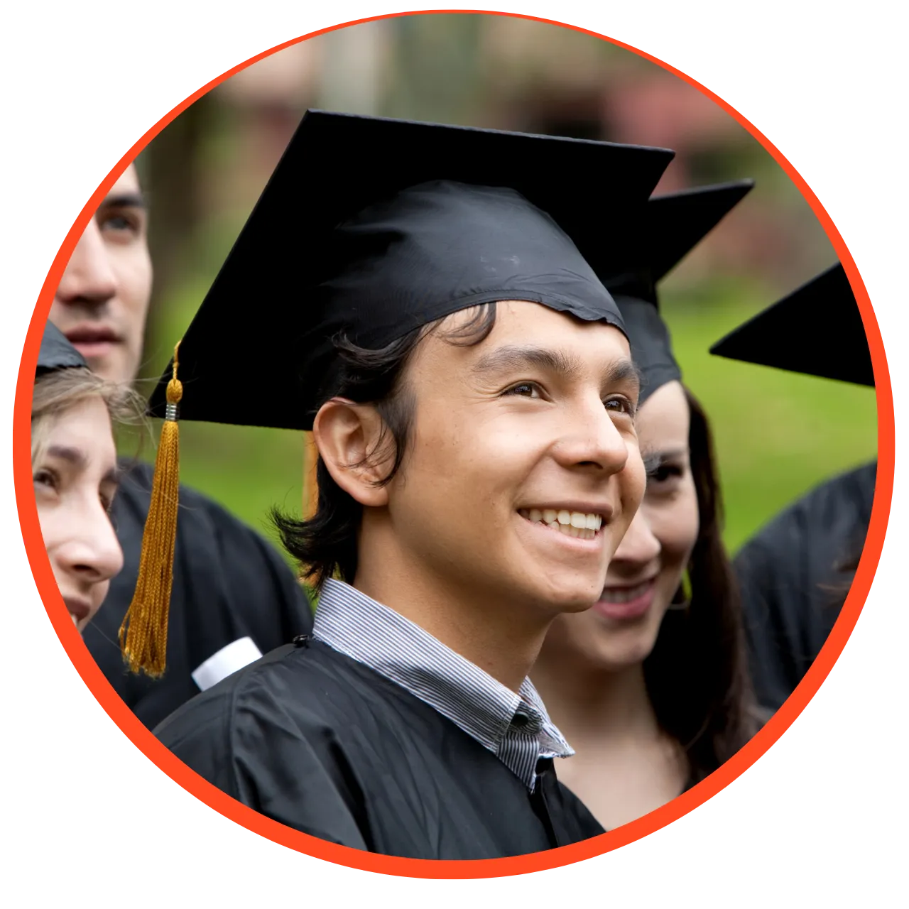 Smiling graduate in a black cap and gown at an outdoor graduation ceremony with peers.