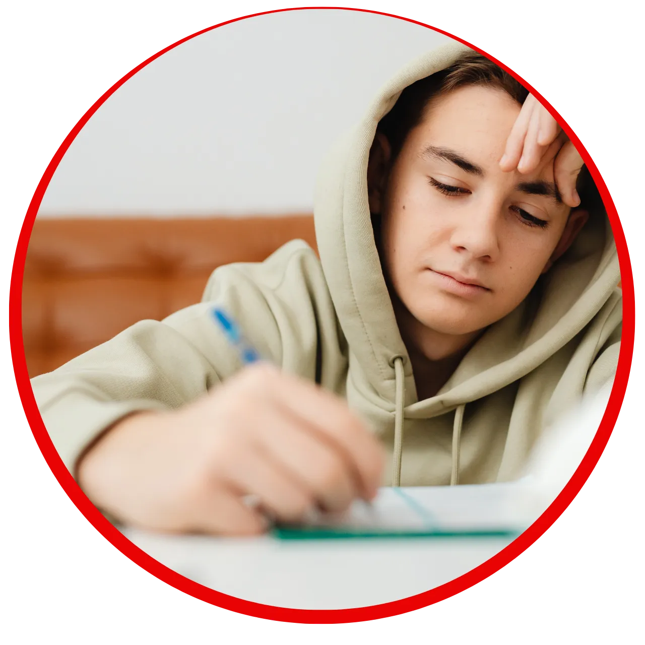 Young person in a beige hoodie concentrating while writing on paper at a table.
