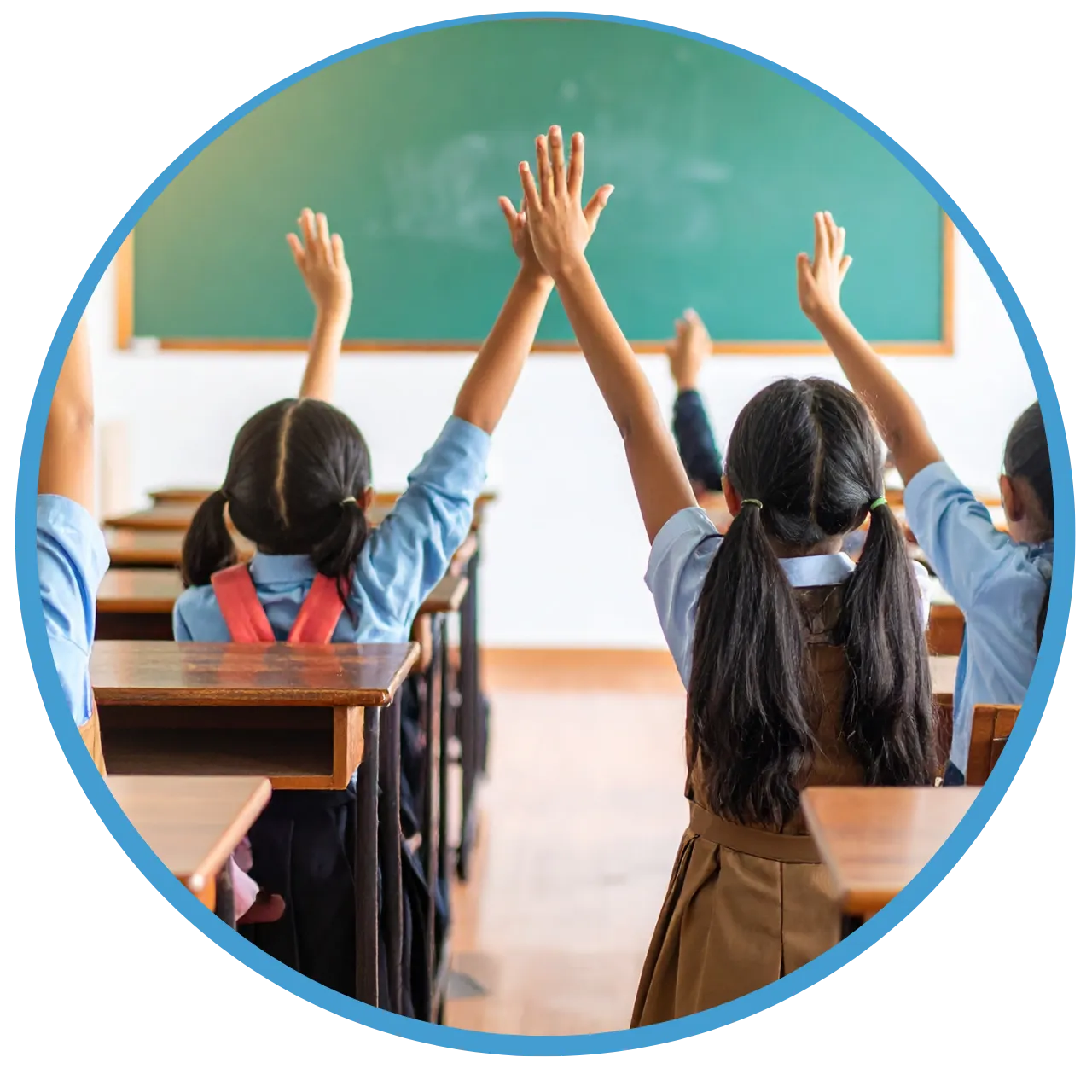 Schoolgirls sitting in classroom desks raising their hands toward a chalkboard.