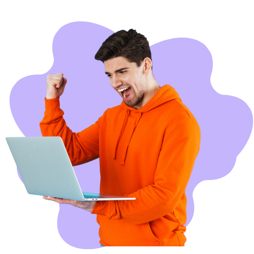 Excited young man in an orange hoodie holding a laptop and raising his fist in celebration.