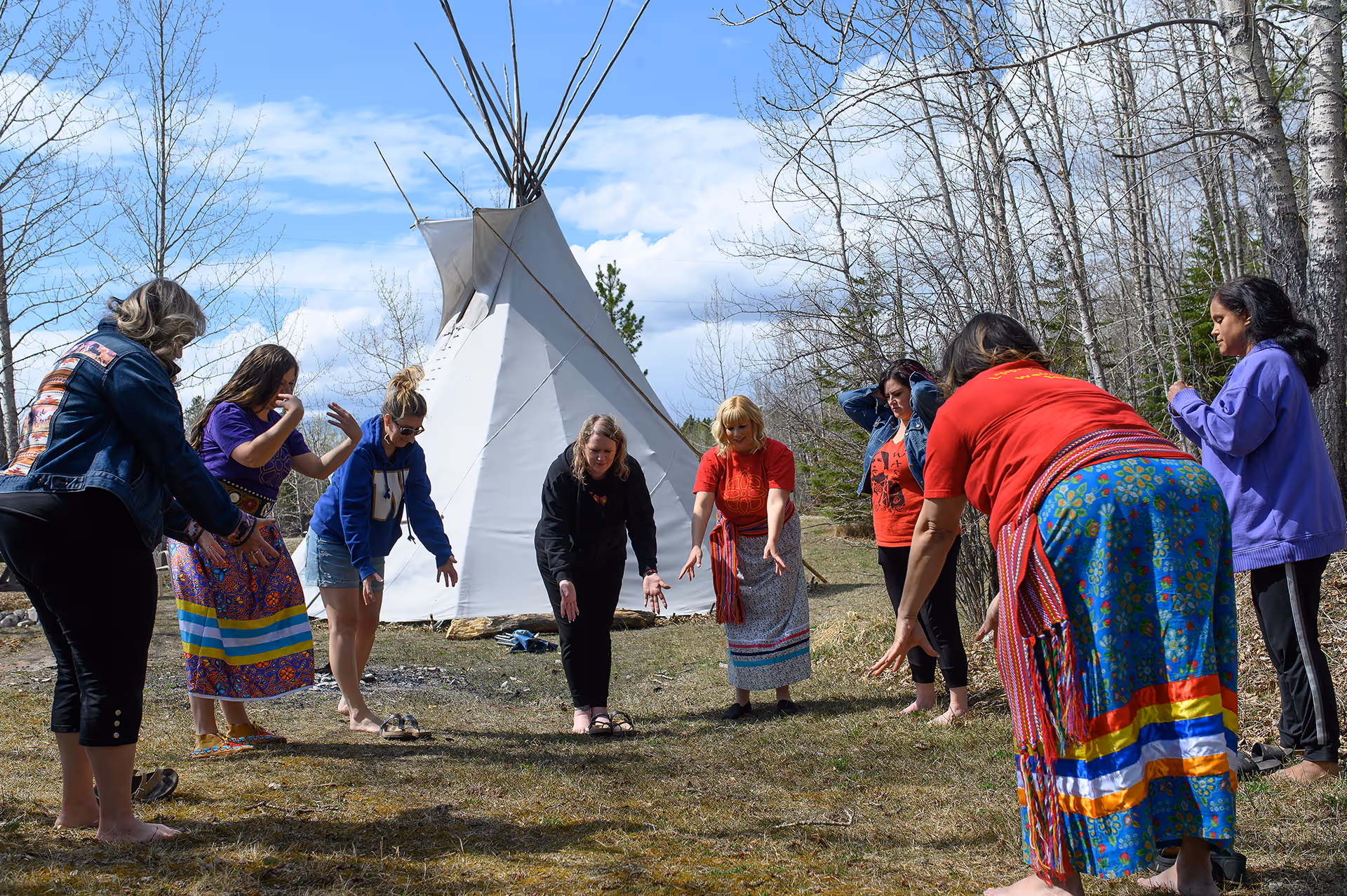 Group of women participating in a land-based wellness activity outside a tipi in a forest