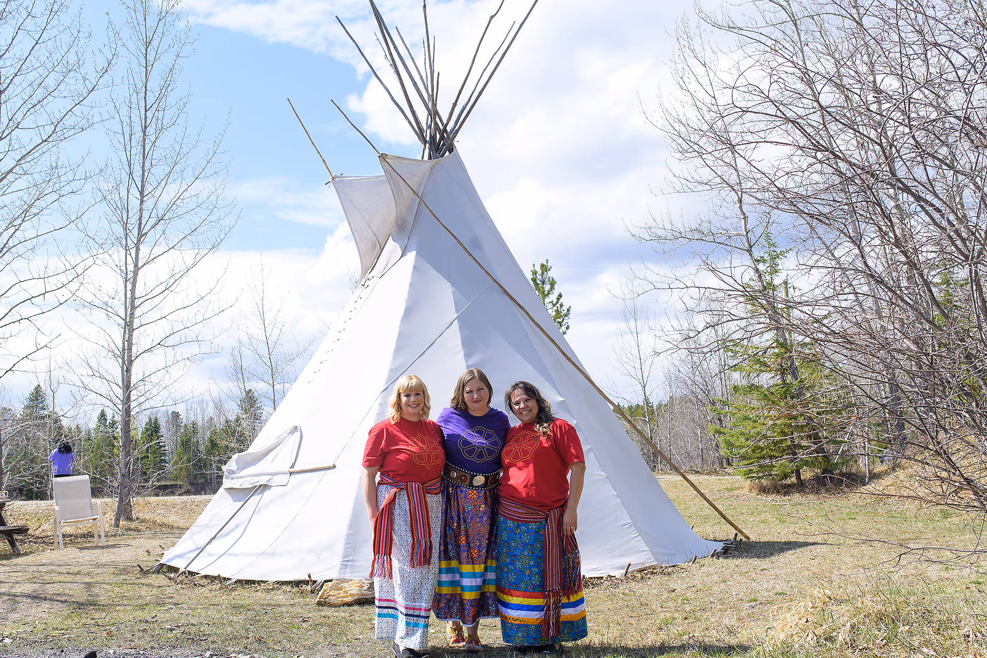 Three cultural wellness facilitators standing together in front of a traditional outdoor teepee