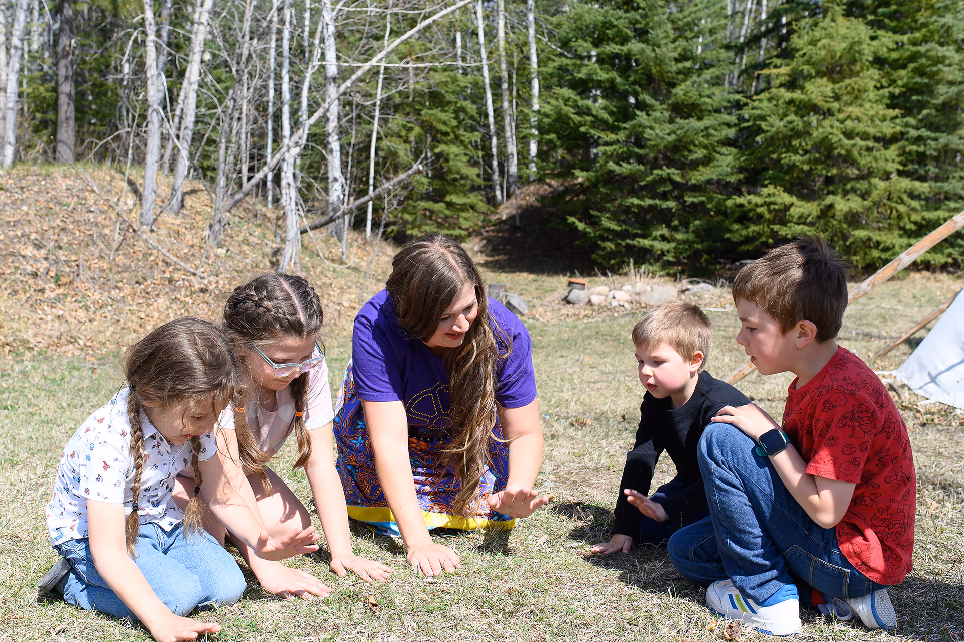 Indigenous wellness facilitator engaging children in a land-based learning activity outdoors