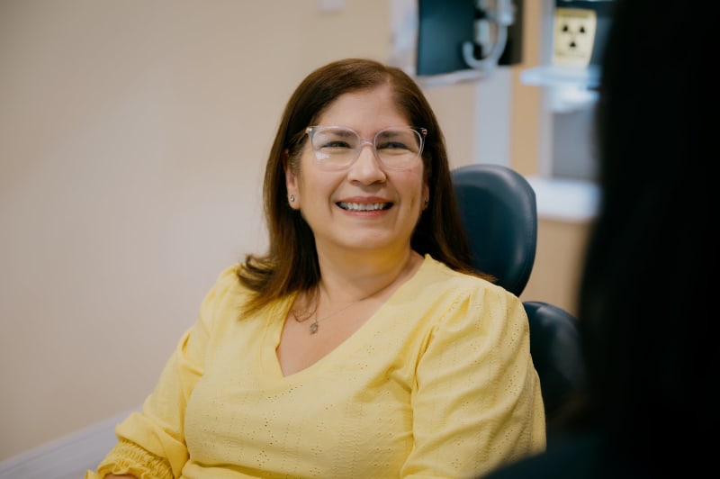 Female dentist smiling warmly in office setting, representing professional dental care provider