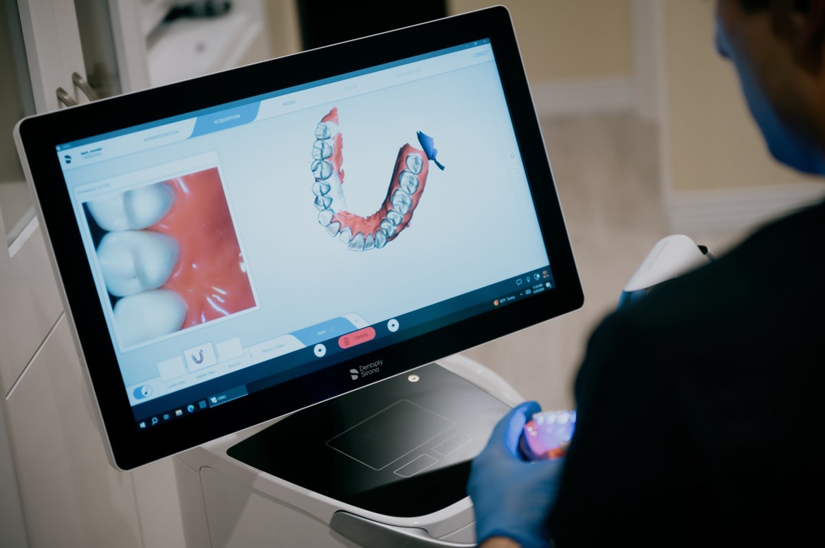 Dental professional examining a 3D scan of teeth and jawbone on computer monitor