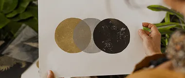 Hand holding a print featuring three overlapping circles in gold, gray, and black with a textured design.