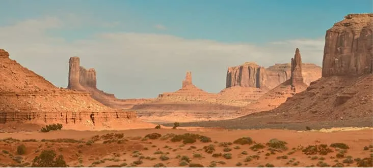 Wide view of a desert landscape with red sandstone rock formations under a blue sky.