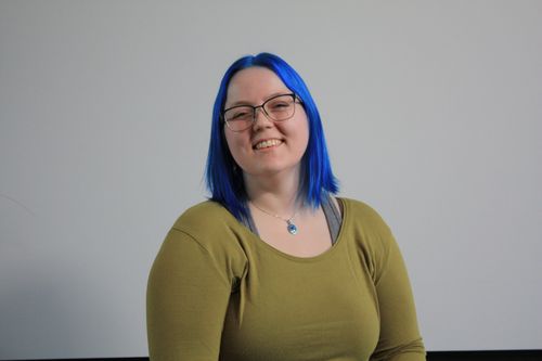 A portrait of Fride Blindheim, a woman with blue hair and a green sweater. She is smiling at the camera.
