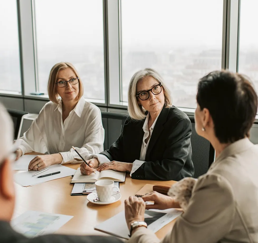 Three professional women in an office having a serious discussion around a table with documents and a coffee cup.