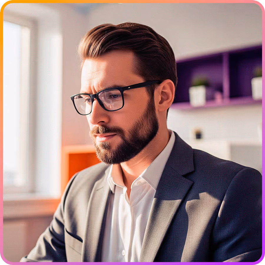 Homem de negócios com barba e óculos, vestido com terno cinza e camiseta branca, trabalhando em escritório moderno.