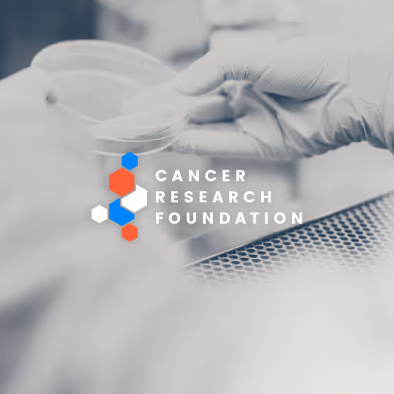 Logo for Cancer Research Foundation with hexagon design in red, blue, and white, overlaid on a photo of gloved hands holding a petri dish in a lab setting.
