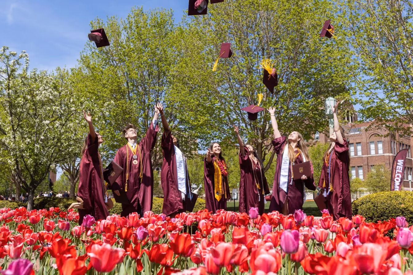 Students in their graduation gowns throwing their caps in the air.