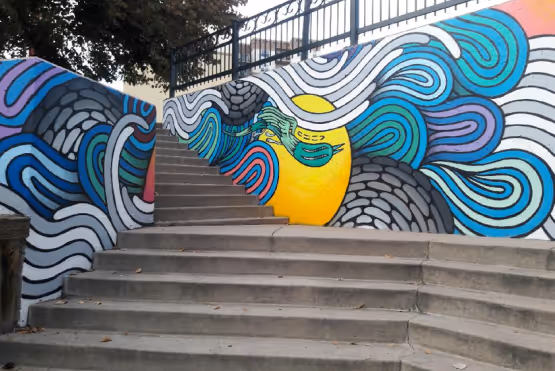 Colorful mural of abstract waves and a yellow sun-like face painted along a stairway.