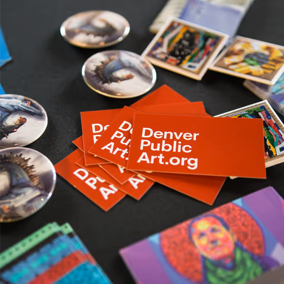 Table display of Denver Public Art promotional items including red stickers, pins, and colorful art prints.