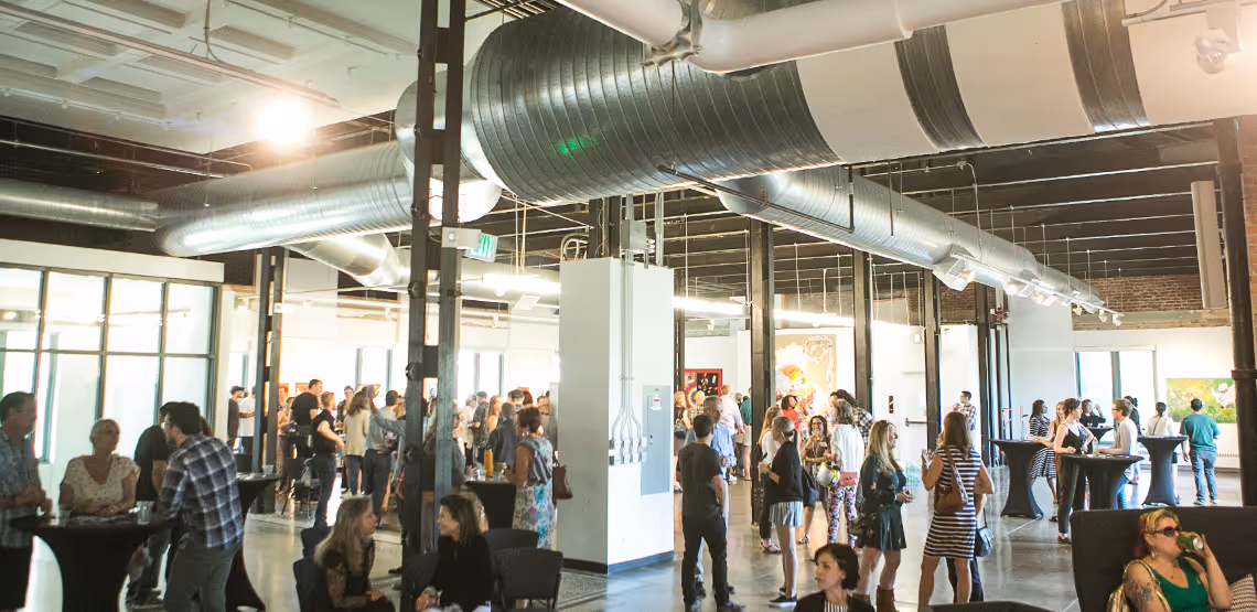 Large crowd gathered in an industrial-style gallery space during a public art event.