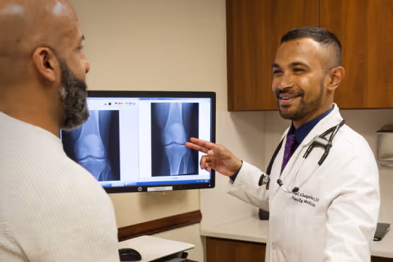 Doctor showing a patient X-ray images of a knee on a computer screen during a consultation.