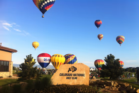 Hot air balloons floating over Colorado National Golf Club with a stone entrance sign in the foreground.