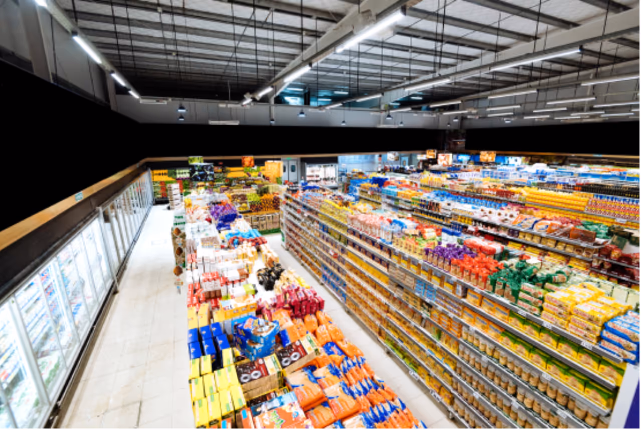 A wide view of a brightly lit supermarket aisle filled with packaged goods and colorful food items.