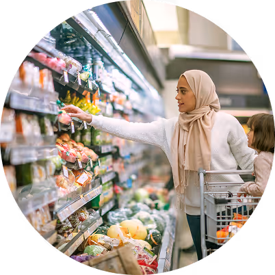 Woman wearing a hijab shopping for fresh produce with a young child seated in the grocery cart.
