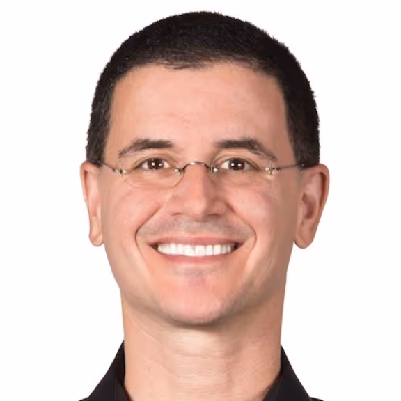 Smiling man with short dark hair and glasses wearing a black shirt against a white background.