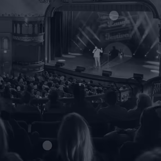 Comedian performing on stage at the Aspen Laugh Festival with an audience watching in a theater.