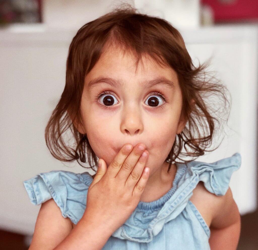 little girl looking surprised covering her mouth