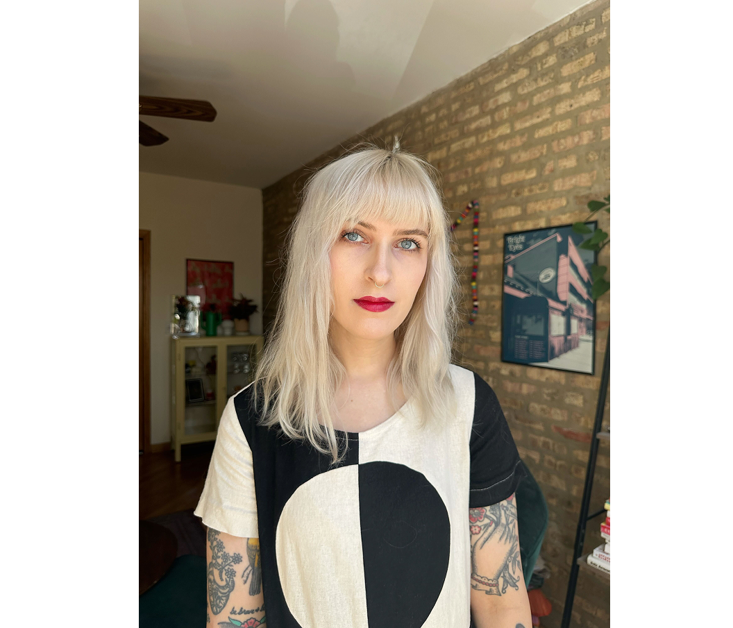 A headshot of a woman with silver-blonde hair and tattoos