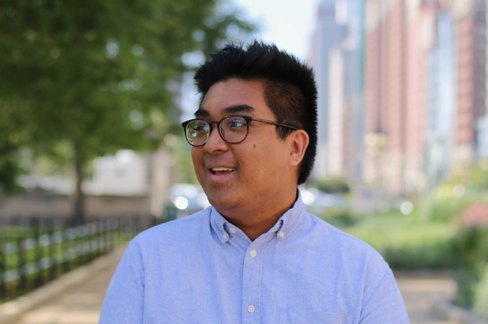 Headshot of a man in a blue shirt standing outside. He is smiling and looking off camera.
