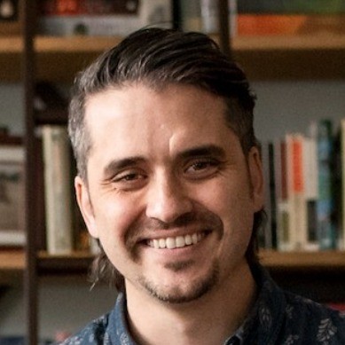 Derek Nelson, co-founder of Clique Studios, smiling in front of a bookshelf