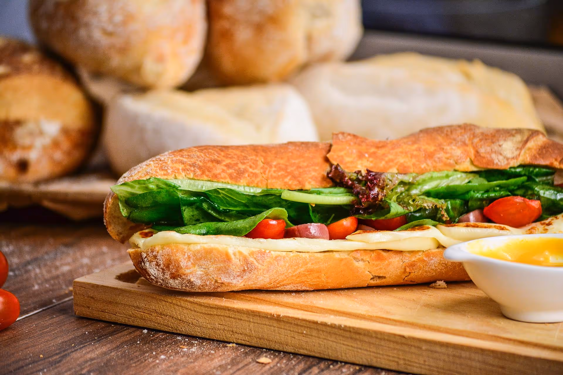 A sandwich with lettuce, tomato, and avocado on a wooden cutting board.