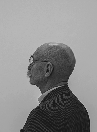 Black and white profile of an elderly bald man with glasses and a mustache wearing a checkered jacket.