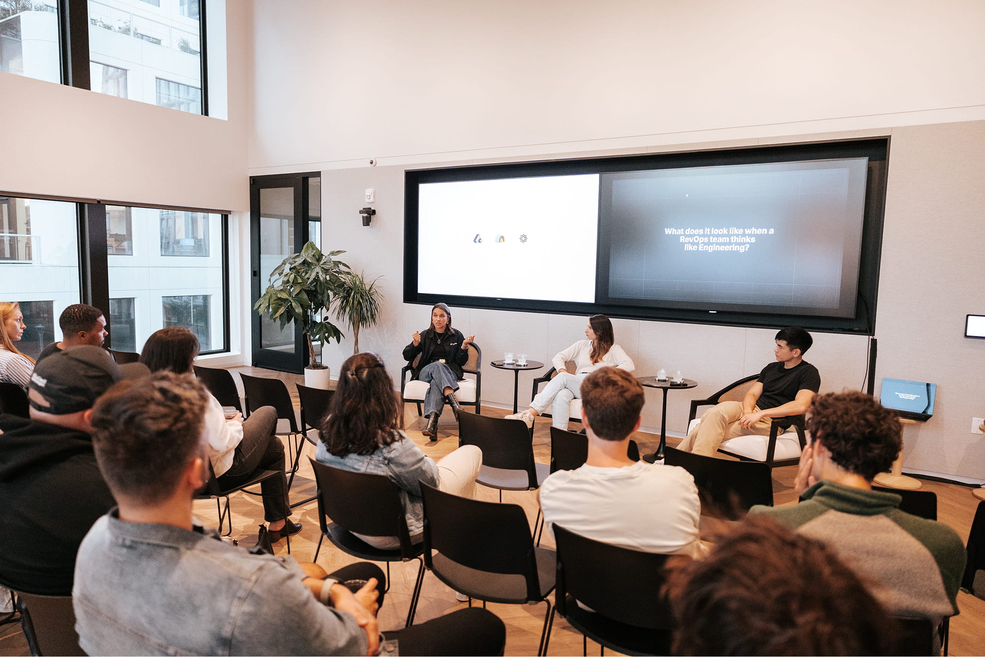 Panel discussion in a modern conference room with three speakers seated in front of an audience and a presentation screen displaying the question about a RevOps team thinking like Engineering.