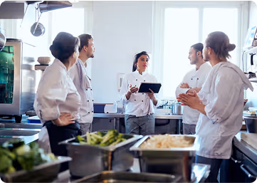 Chef leading a team meeting in a commercial kitchen.