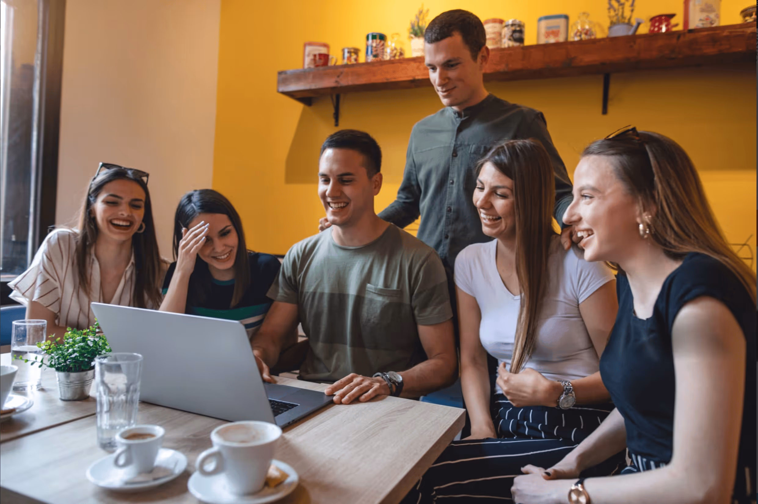 Group of friends smiling and watching laptop together in café.