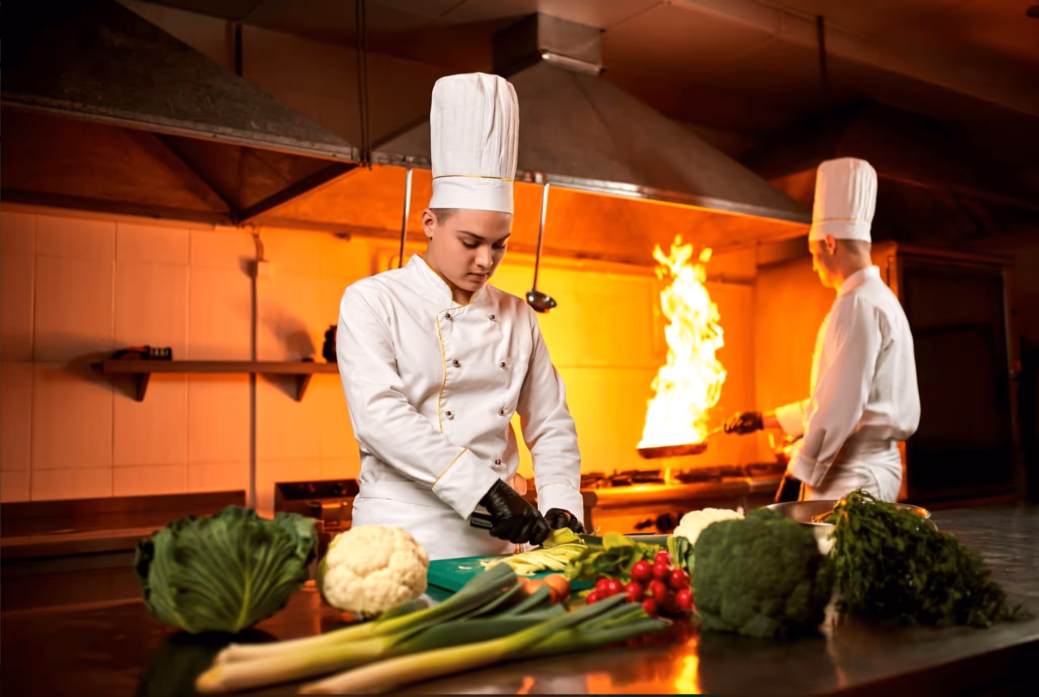 Chefs cooking in a kitchen with fresh vegetables and flames.
