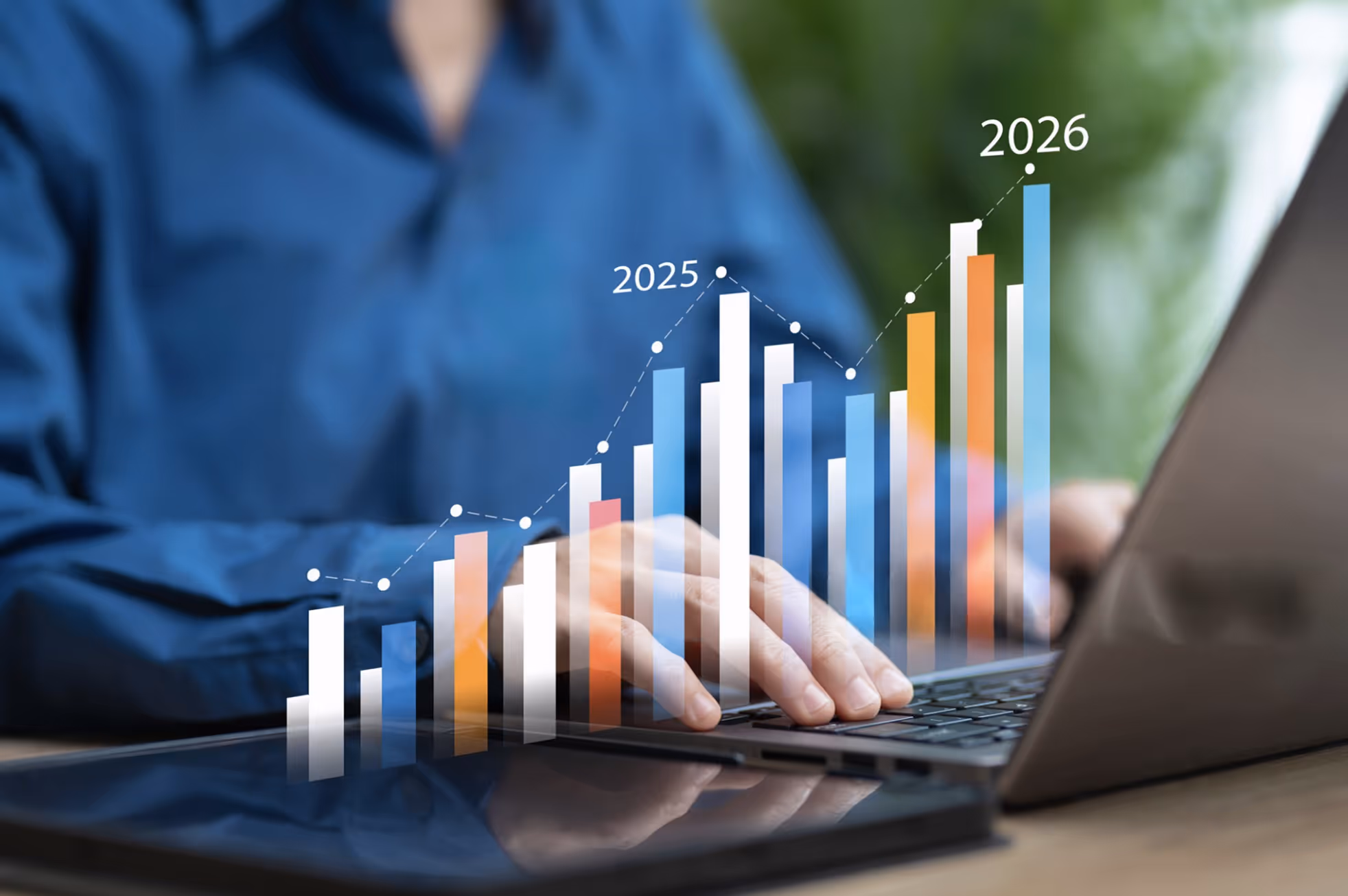 Hands typing on a laptop keyboard with a rising bar chart showing data trends for 2025 and 2026.
