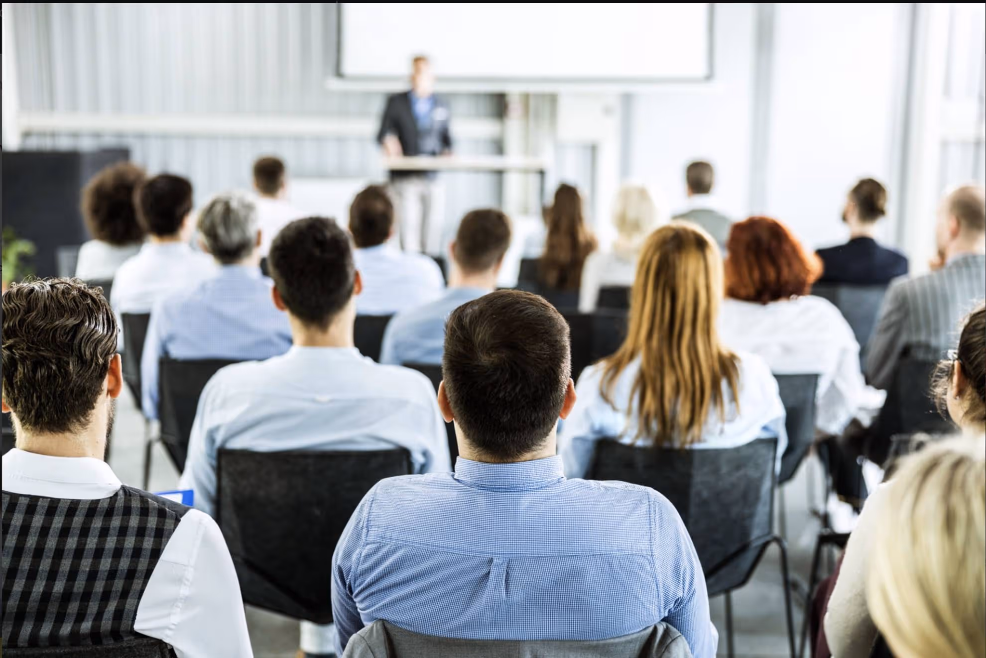 Group of adults seated and facing a speaker presenting in a classroom or training room.