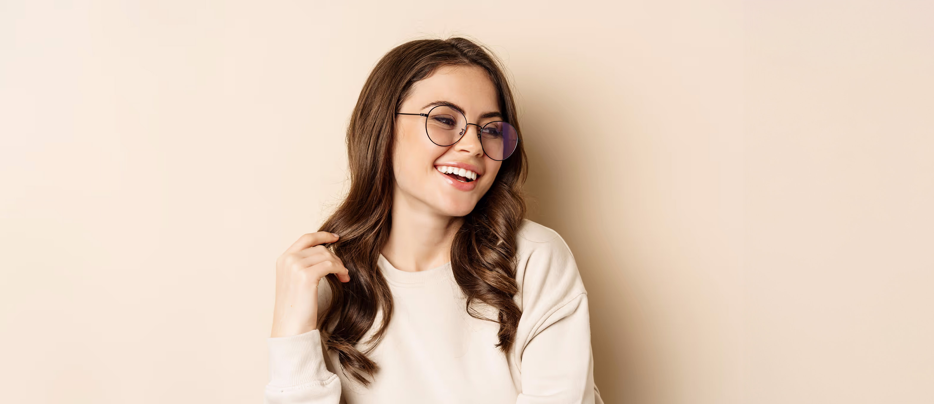 Smiling woman with glasses touching hair, wearing white sweater