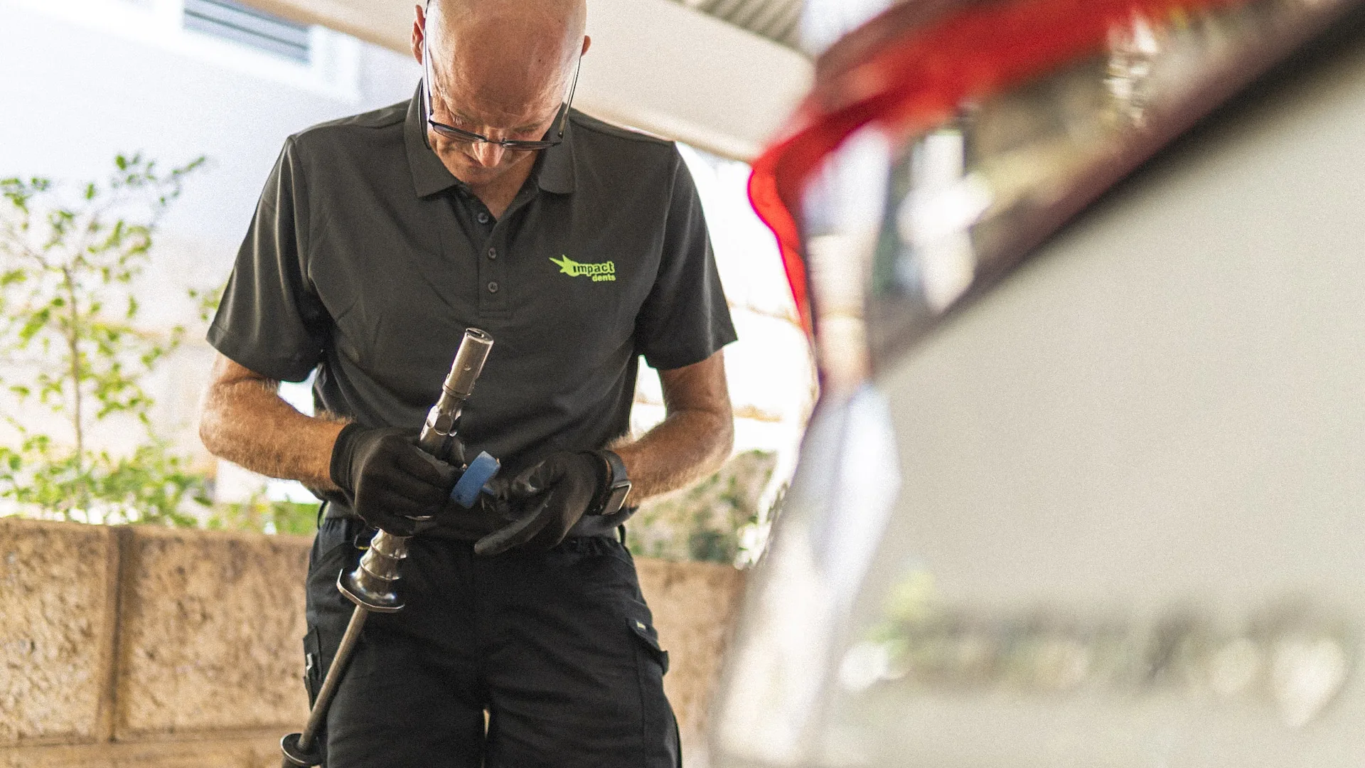 Mark from Impact Dents holding a paintless dent repair tool beside a white vehicle
