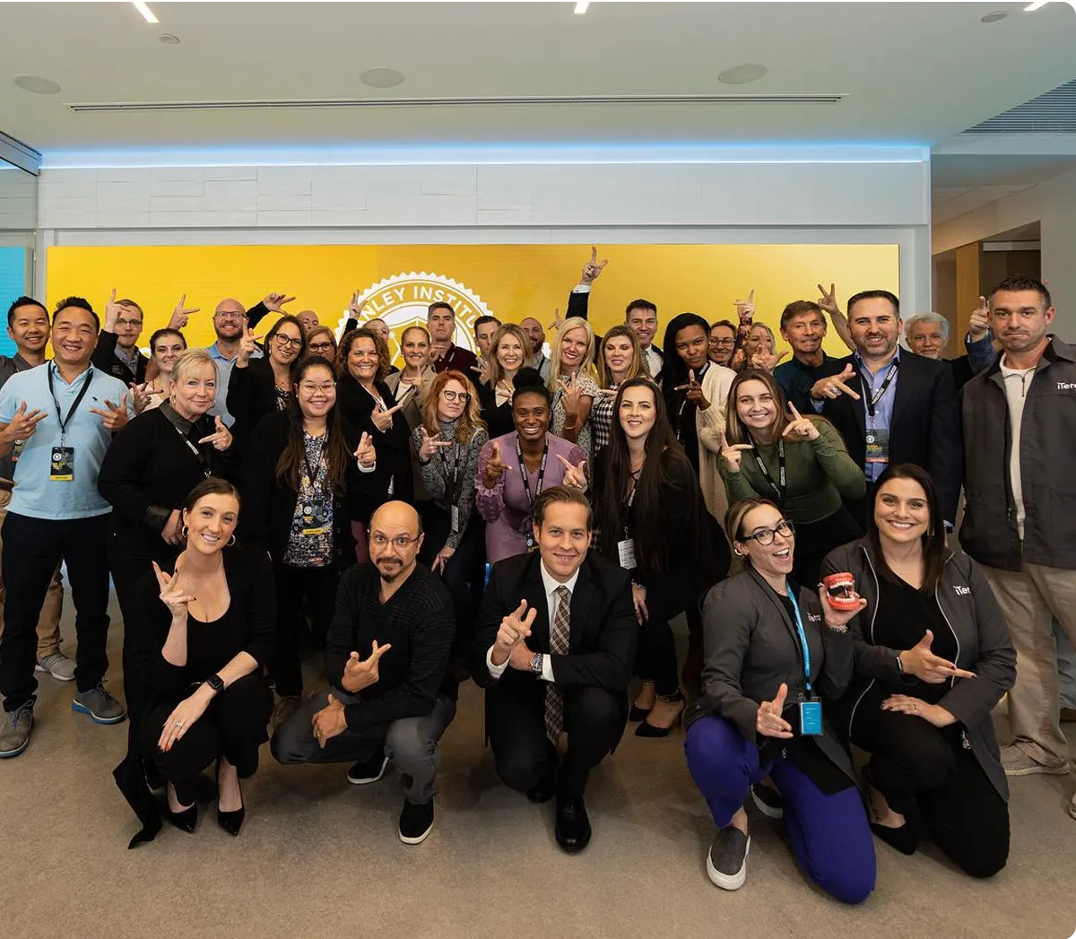 Large group photo of team members posing with hand gestures in office