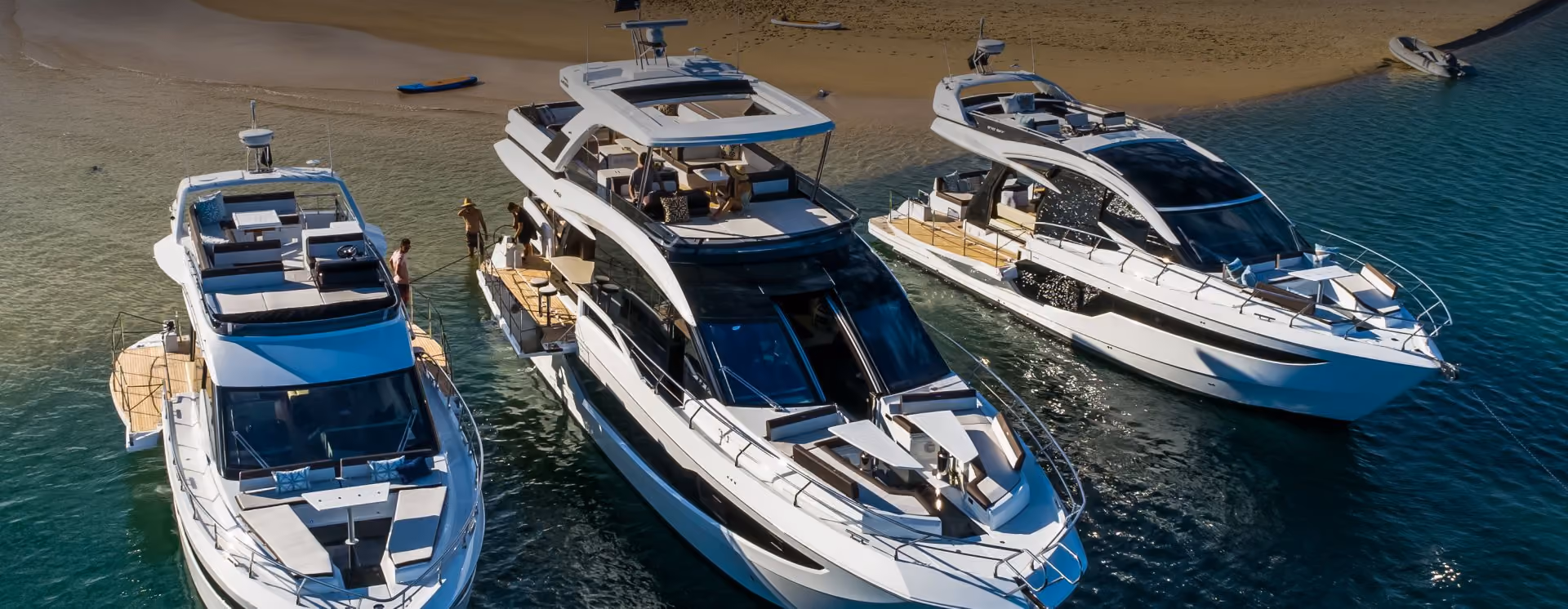 Three galeon yachts anchored off the shore of a sand bar with people in the water.